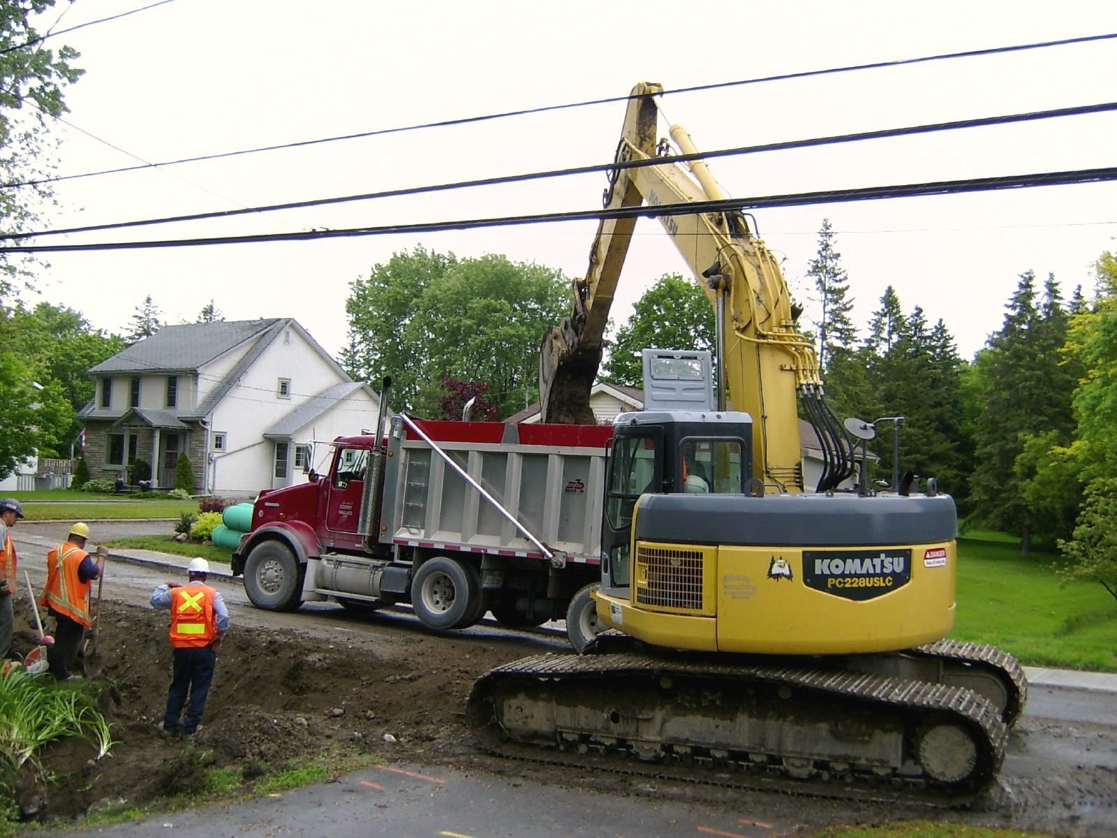 An excavator and dump truck working on a trench in front of a white house