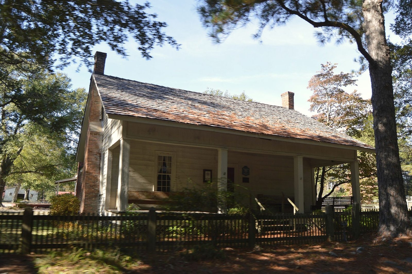 A white wooden farmhouse with a deep front porch under pine trees