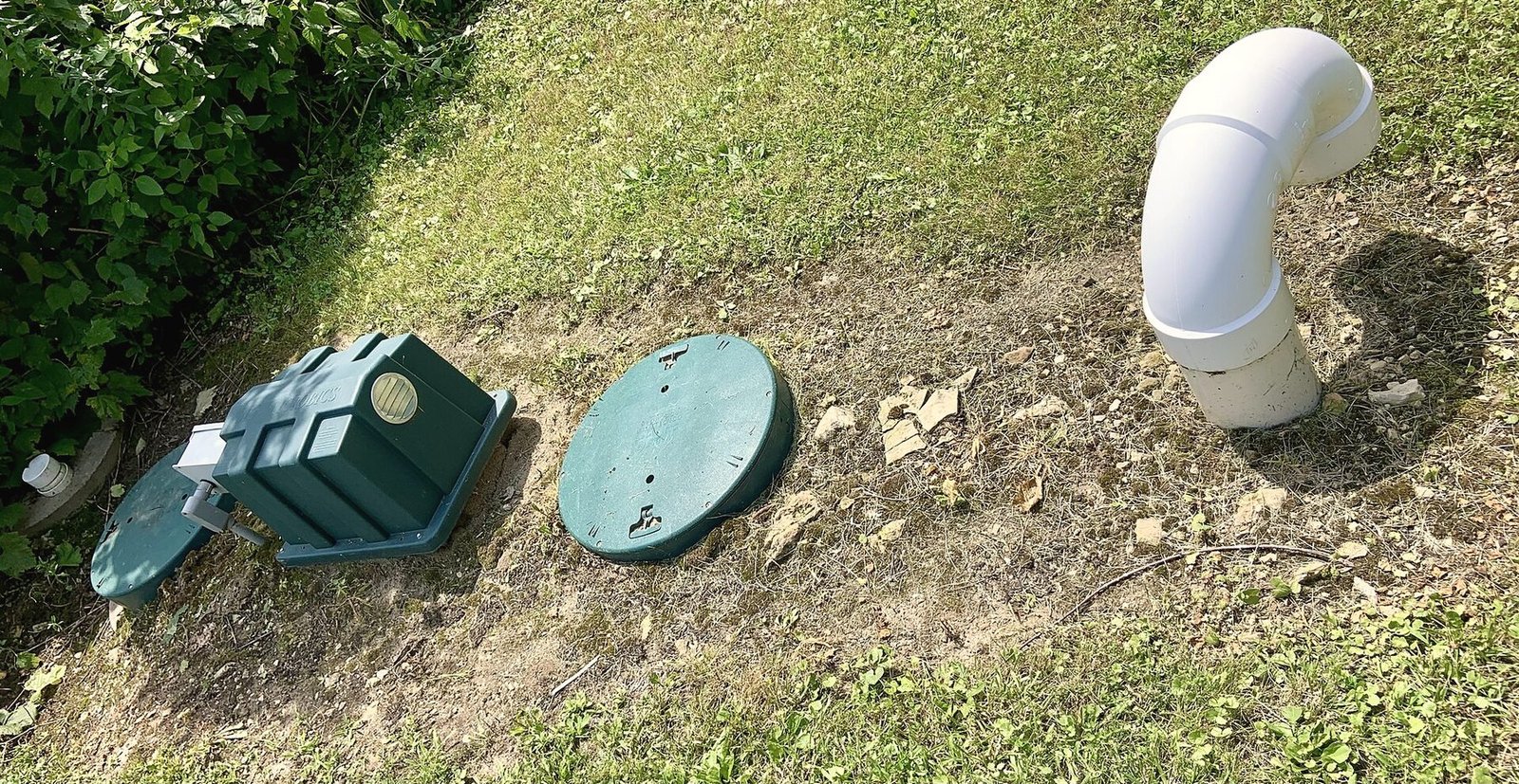 Two green septic access lids and a white cleanout pipe in a sloped lawn
