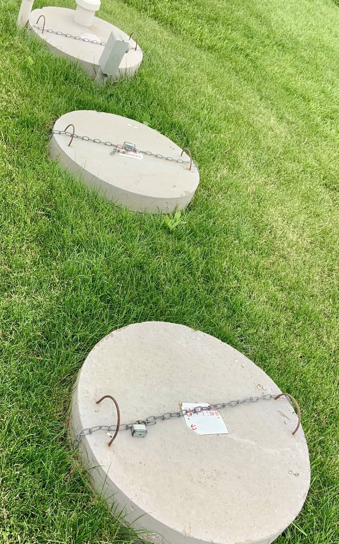 Three round concrete lids in a row in a grassy bank