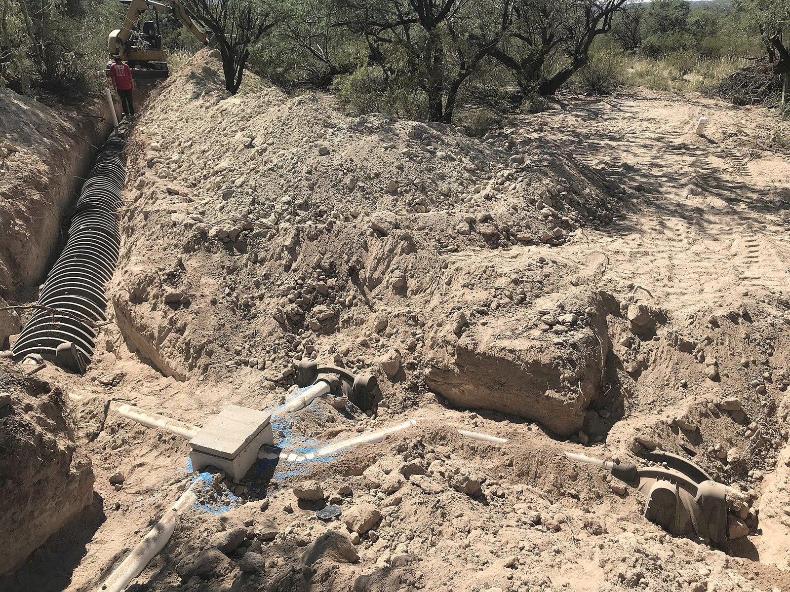An open trench in pale sandy soil with drain field pipe laid in the bottom