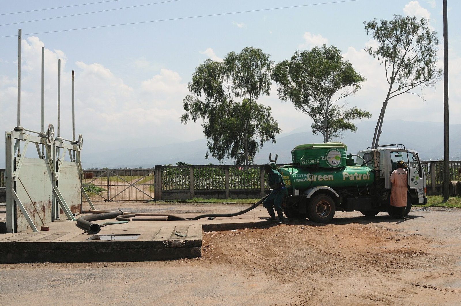 A green vacuum tanker truck discharging through a hose at a treatment yard